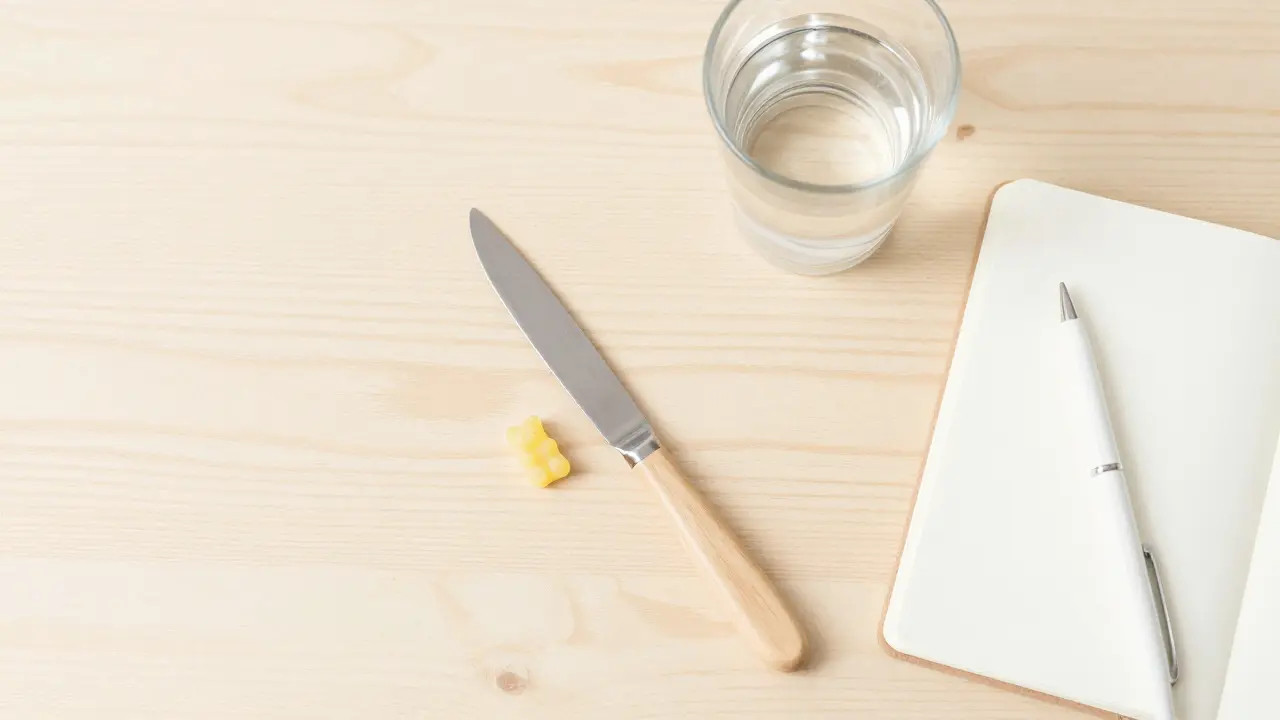 Ein halbiertes CBD-Gummibärchen auf einem hellen Holztisch neben einem Notizbuch.